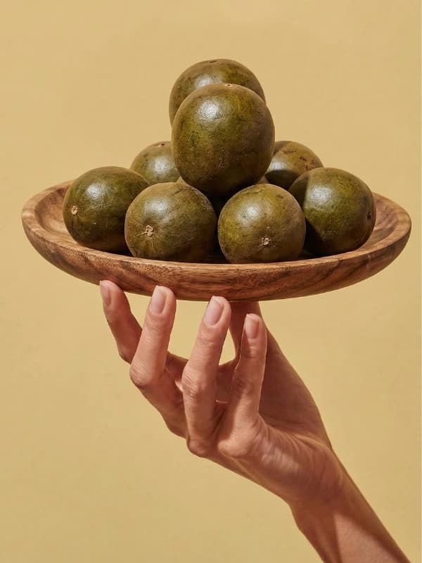Hand holding a wooden bowl filled with fresh monk fruit - the natural sweetener used in Purely U products